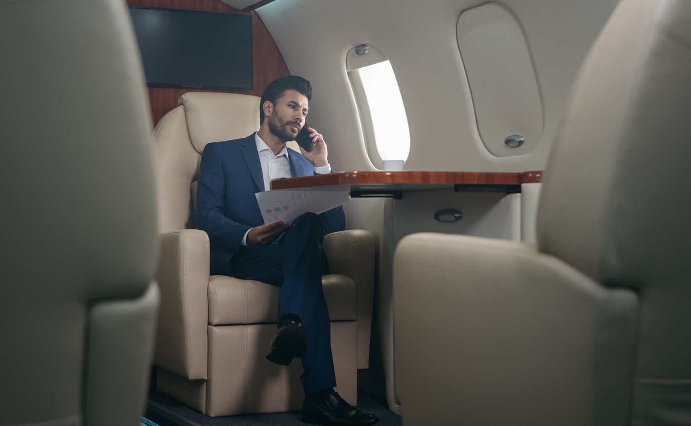 pensive middle eastern businessman talking on mobile phone, holding financial report working with documents sitting in plane