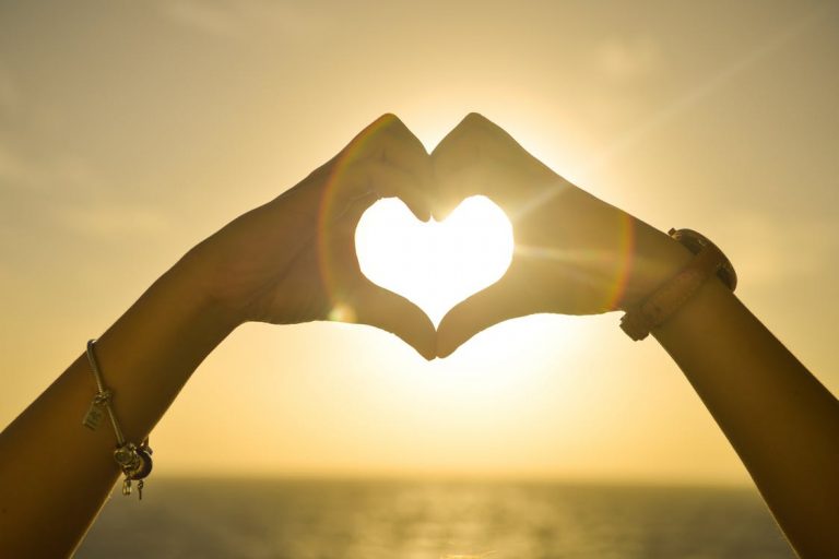 hand forming heart on sunrise