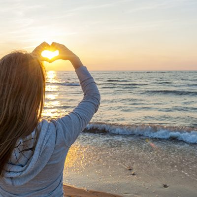 woman on the beach with heart hand sign