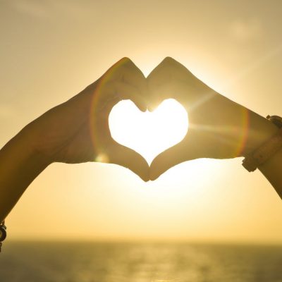 hand forming heart on sunrise